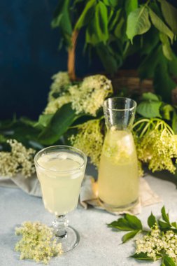 Elderflower şurubundan buz küpleri, açık gri bir masa yüzeyinde bir bardakta meyve suyu veya şampanya, seçilmiş odak noktası, dar bir alan derinliği