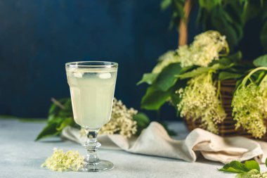 Elderflower şurubundan buz küpleri, açık gri bir masa yüzeyinde bir bardakta meyve suyu veya şampanya, seçilmiş odak noktası, dar bir alan derinliği