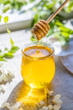 Tatlı bal kavanozu bahar akasyası çiçeklerini sarmıştı. Kavanozdaki kaşıktan bal akar. Güneşli ışık, alanın sığ derinliği.