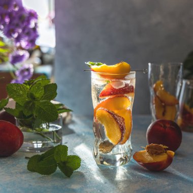 Soğuk şeftalili kokteyl ya da naneli buzlu çay. Güneşli ışık, açık beton masa yüzeyi. Alanın sığ derinliği, kapat, metin için alanı kopyala.