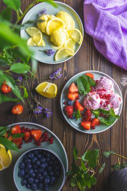 Farklı dondurma şerbeti. Limon ve lavanta, çilek, kırmızı frenk üzümü ve ahşap masa yüzeyindeki tabaklarda yabanmersinli dondurma. Koyu kırsal tarzı.