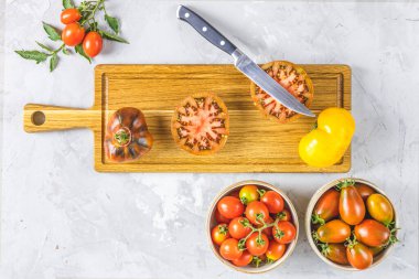 Çiğ taze domates dilimler. Ahşap kesme tahtasının üzerinde renkli domatesler ve mutfak bıçağı. Yeşil ev yaşam tarzı ve geçimlik tarım ürünleri kavramı açık gri beton yüzeyde yatıyordu.