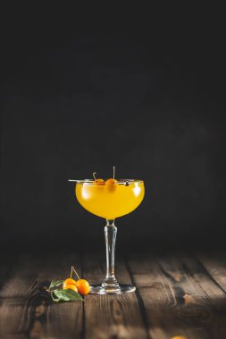 Şampanya kadehindeki karıştırıcıdan erik cini ve tonik kokteyli. Sarı taze erik koyu ahşap masa yüzeyi.