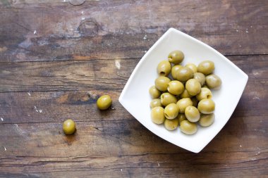Green olives in wight plant on wooden table, selective focus