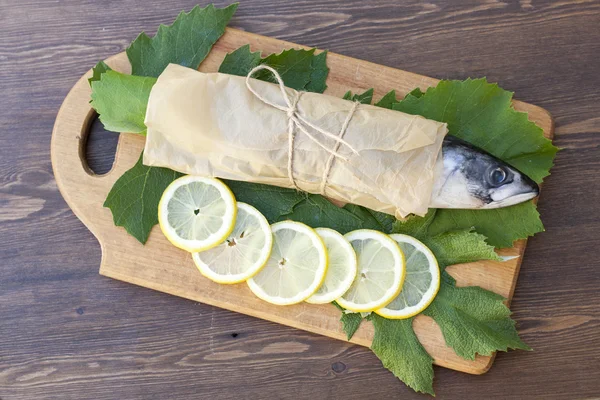 Cavala fresca sobre papel em folhas de uva com fatias de limão — Fotografia de Stock