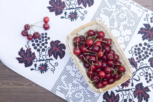 Fresh cherries on embroidered towel in wooden table