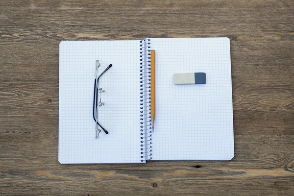 Élargir le bloc-notes en spirale dans une cellule avec un stylo, un crayon, une gomme et des lunettes sur une table en bois, mise au point sélective — Photo