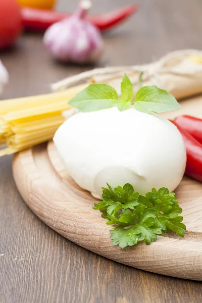 Mozzarella with herbs, noodles, fresh vegetables, chilli, garlic on a wooden round board, selective focus — Stock Photo, Image