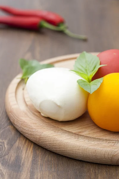 Mozzarella with herbs, fresh vegetables, chilli on a wooden round board, selective focus — Stock Photo, Image