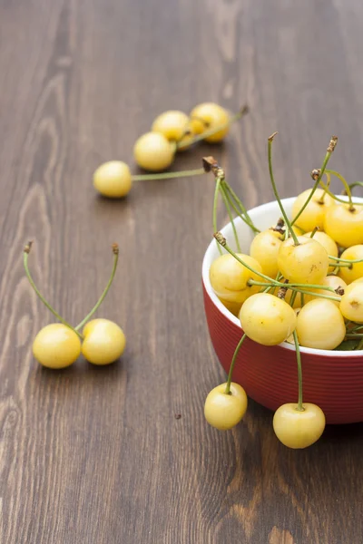 Fresh yellow cherry in a red bowl on a wooden background — Stock Photo, Image