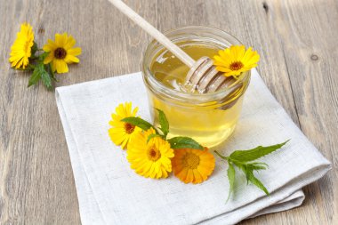Linden honey in jar and calendula blossoms on wooden table, selective focus