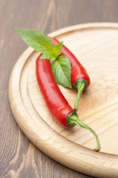 Red chilli pepper with green basil on wooden board, selective focus — Stok fotoğraf