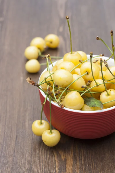 Fresh yellow cherry in a red bowl on a wooden background, selective focus — 图库照片
