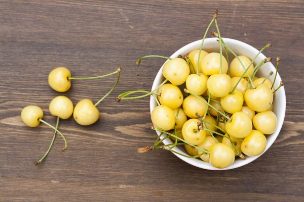 Fresh yellow cherry in a red bowl on a wooden background, selective focus — Stock fotografie