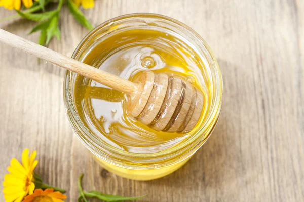 Linden honey in jar and calendula blossoms on wooden table, selective focus — Stock Fotó