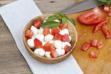 Sliced tomatoes, basil and mozzarella cheese on a wooden plate, selective focus
