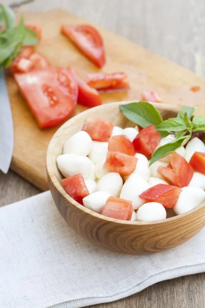 Sliced tomatoes, basil and mozzarella cheese on a wooden plate, selective focus — Stock Photo, Image