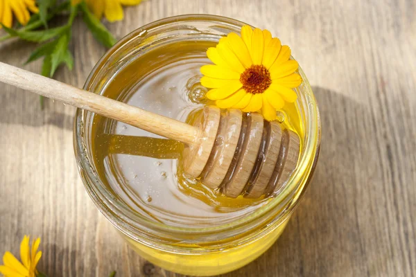 Linden honey in jar and calendula blossoms on wooden table, selective focus — Stock Fotó