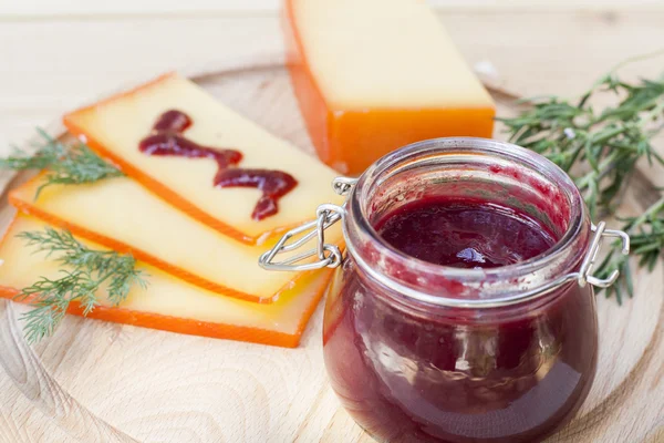 Нарезанный сыр и вишневый соус на деревянной доске с укропом и розмарином — стоковое фото