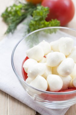 Mozzarella cheese in a glass bowl, tomatoes, sliced tomatoes and herbs on a wooden table, selective focus