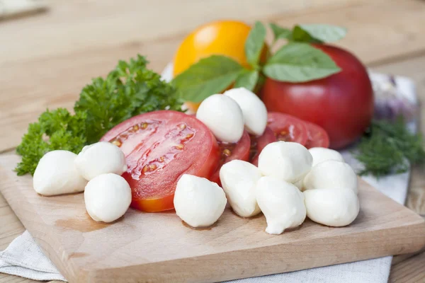 Sliced tomatoes, basil and mozzarella cheese on a wooden board, selective focus — Stock Photo, Image