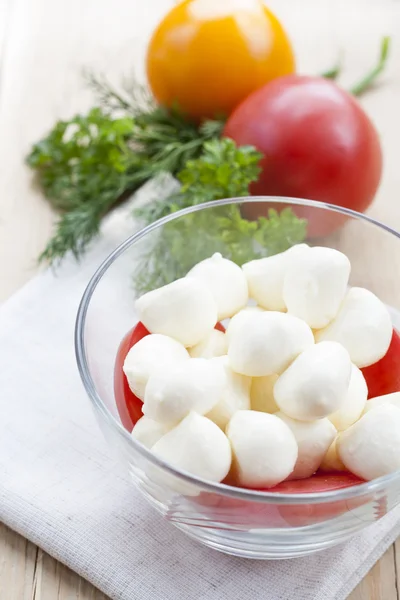 Mozzarella cheese in a glass bowl, tomatoes, sliced tomatoes and herbs on a wooden table, selective focus — Zdjęcie stockowe