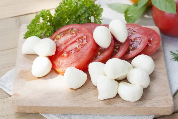 Sliced tomatoes, basil and mozzarella cheese on a wooden board, selective focus — Stock Photo, Image