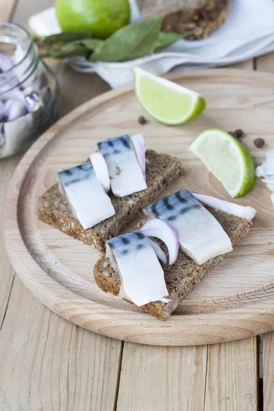 Slices of marinated mackerel with onion in a jar, lime, laurel and bread on wooden board, selective focus — Φωτογραφία Αρχείου