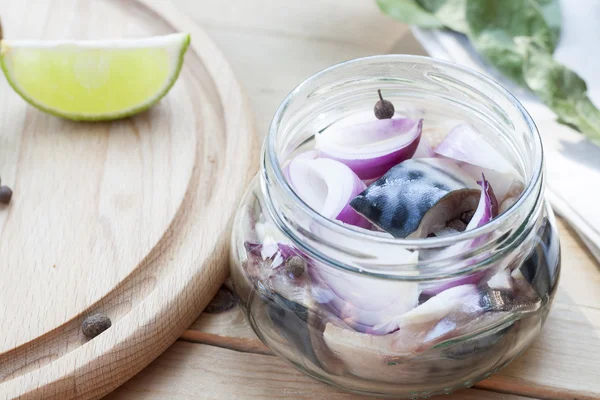 Slices of marinated mackerel with onion in a jar, lime, laurel and bread on wooden board, selective focus
