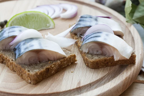 Slices of marinated mackerel with onion in a jar, lime, laurel and bread on wooden board, selective focus
