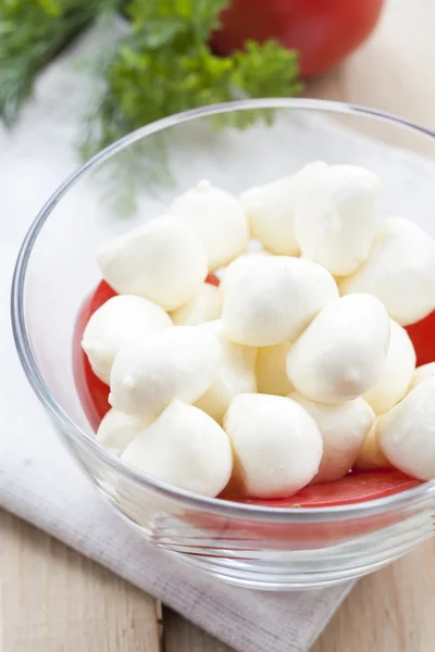 Mozzarella cheese in a glass bowl, tomatoes, sliced tomatoes and herbs on a wooden table, selective focus — ストック写真