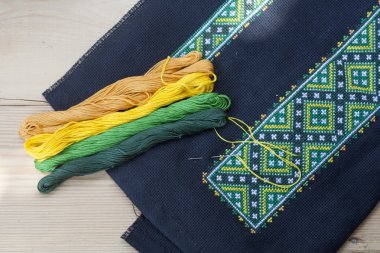 Ukrainian embroidery on the black fabric and thread embroidery on a light wooden table, selective focus