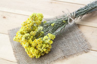 Dwarf everlast flowers bouquet, napkin and twine bobbin on light wooden table, selective focus