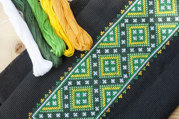 Ukrainian embroidery on the black fabric and thread embroidery on a light wooden table, selective focus — стокове фото