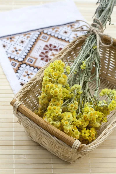 Dwarf everlast flowers bouquet in a wicker basket and napkin with embroidery on light wooden table, selective focus — Stockfoto