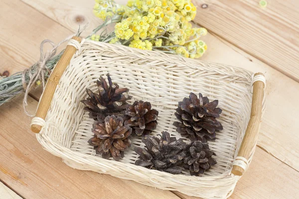 Dwerg everlast bloemen boeket en pine kegels in een rieten mand op licht houten tafel, selectieve aandacht — Stockfoto