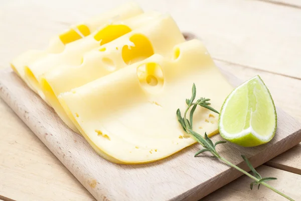 Maasdam várias fatias de queijo em tábua de madeira, limão e alecrim — Fotografia de Stock
