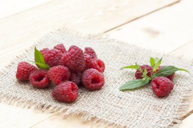 Fresh sweet red raspberry and mint on light wooden table, selective focus