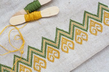 Ukrainian embroidery on the linen fabric and thread embroidery on a wooden table, selective focus