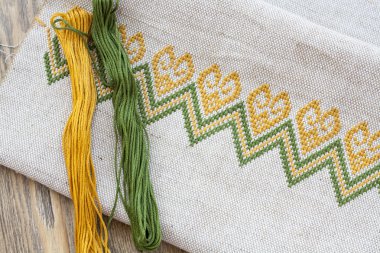 Ukrainian embroidery on the linen fabric and thread embroidery on a wooden table, selective focus