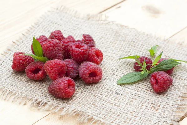 Fresh sweet red raspberry and mint on light wooden table, selective focus