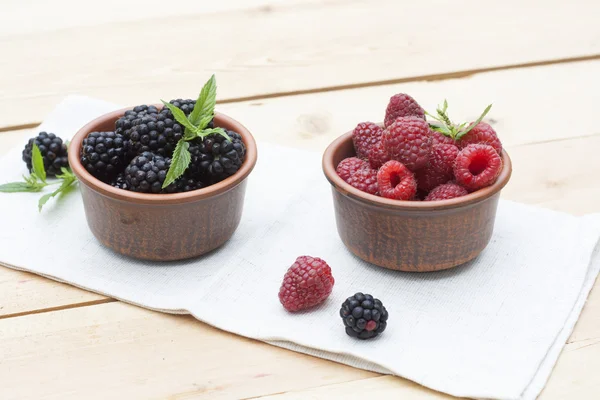 Fresh sweet red raspberry and blueberries in a clay pot and mint on light wooden table, selective focus — Stock Photo, Image