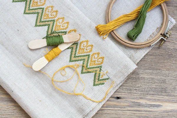 Ukrainian embroidery on the linen fabric and thread embroidery on a wooden table, selective focus — Stockfoto