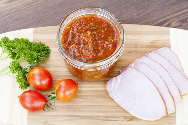 Homemade tomato sauce in glass jar with tasty ham smoked whole and sliced close-up, selective focus — Stock Fotó