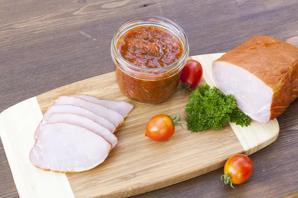 Homemade tomato sauce in glass jar with tasty ham smoked whole and sliced close-up, selective focus — Stockfoto