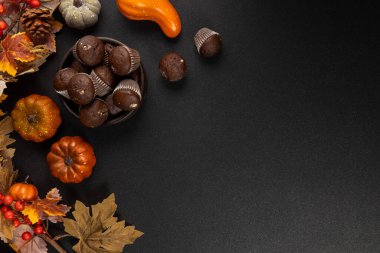 Chocolate muffins arranged in a bowl with autumn leaves, small pumpkins and berries on a dark background  cozy flat lay for harvest, thanksgiving and halloween themes