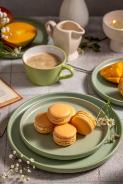 Lezzetli badem kurabiyeleri, taze mango dilimleri ve masada narin papatyalar ve açık bir kitapla hazırlanmış sıcak bir fincan kahveyle serinletici bir kahvaltı.