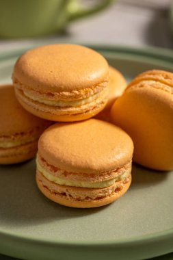 Narin kabuklu ve kremalı turuncu badem kurabiyeleri yeşil seramik bir tabakta sergileniyor. Tatlı Fransız tatlıları ve gurme tatlılarını temsil ediyor.