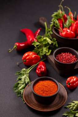 Dark background showcasing vibrant red chili peppers, habanero peppers, fresh parsley, and bowls of powdered paprika and pink peppercorns, providing essential ingredients for spicy food and cooking