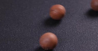 Kabuklu fındıklar yuvarlanıyor, zıplıyor ve ağır çekimde dönüyor kaba, karanlık bir arkaplanda soyut ve dinamik bir yemek temalı video yaratıyor.